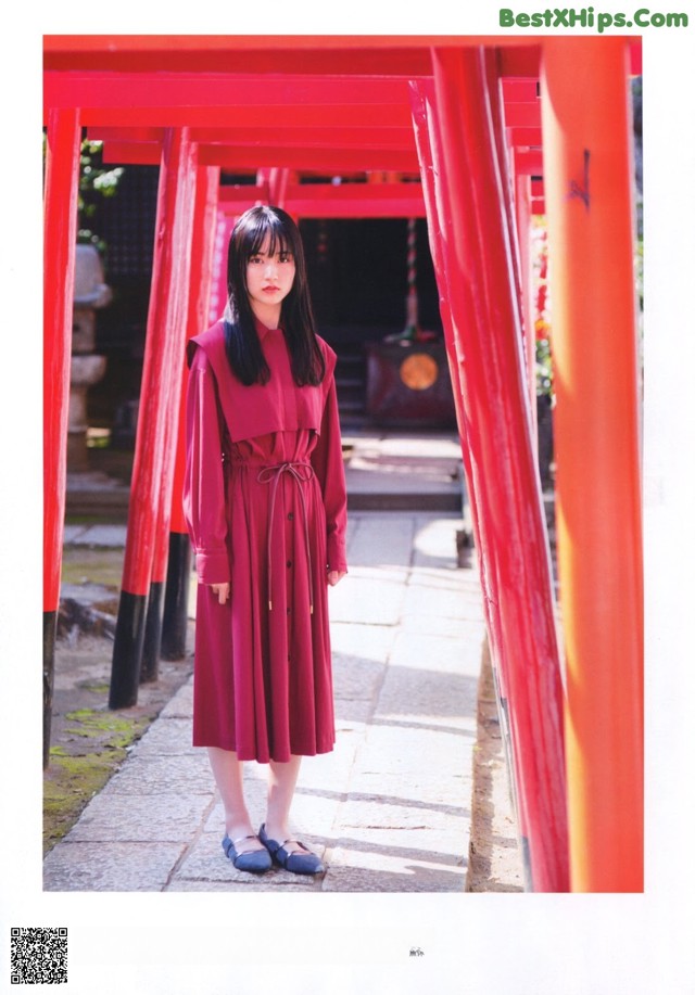 A woman in a red dress standing in front of red pillars.