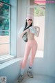 A woman in a white shirt and pink leggings posing by a window.