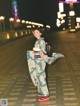 A woman in a kimono standing on a sidewalk at night.