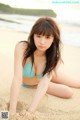 A woman in a blue bikini sitting on the beach.