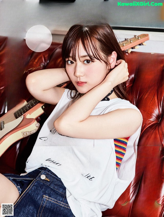 A woman sitting on a red couch with a guitar.
