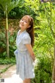 A woman in a blue and white dress standing next to a tree.