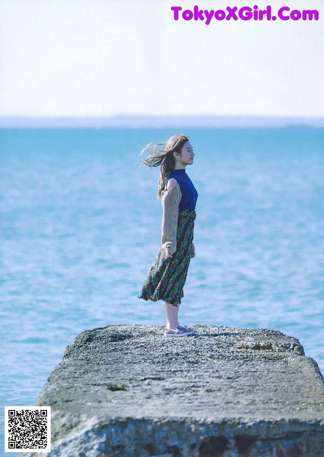 A woman standing on a rock by the ocean.